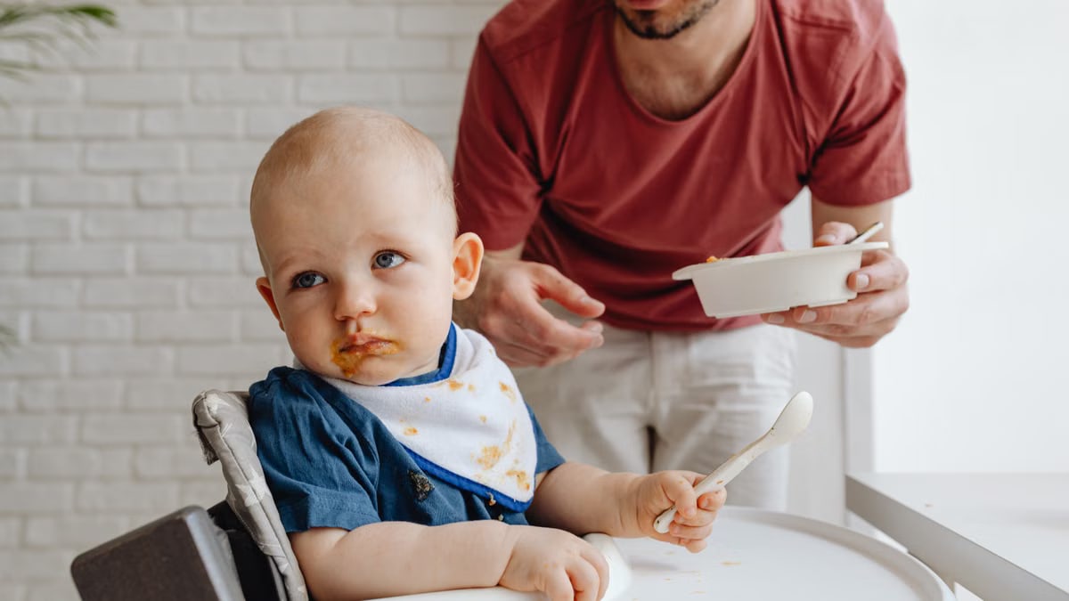 A father feeding his baby in a high chair, showcasing a nurturing family moment.